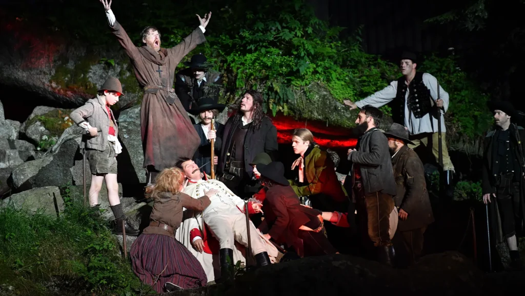 Man in Mönchskluft schreit mit weiteren Darstellern auf einer Bühne
