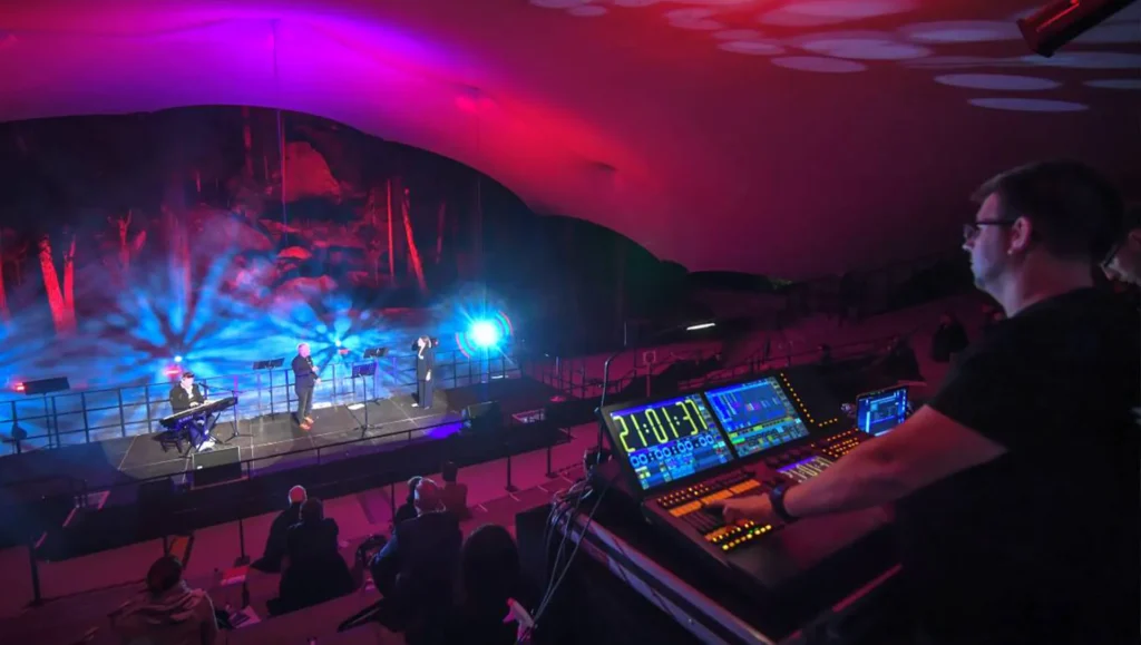 Mann an Mischpult blickt auf eine Bühne