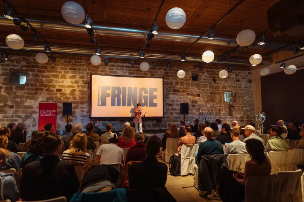 Person steht auf einer Bühne mit viele Zuhörern