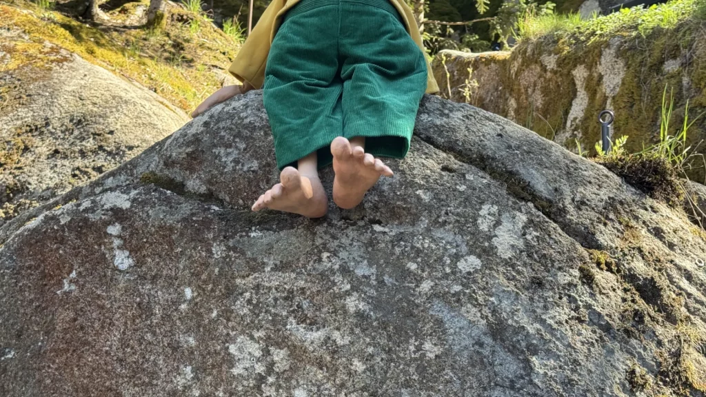 Das Foto zeigt die Pumuckl Puppe ab der Grütellinie, wie sie auf einem Felsen sitzt.